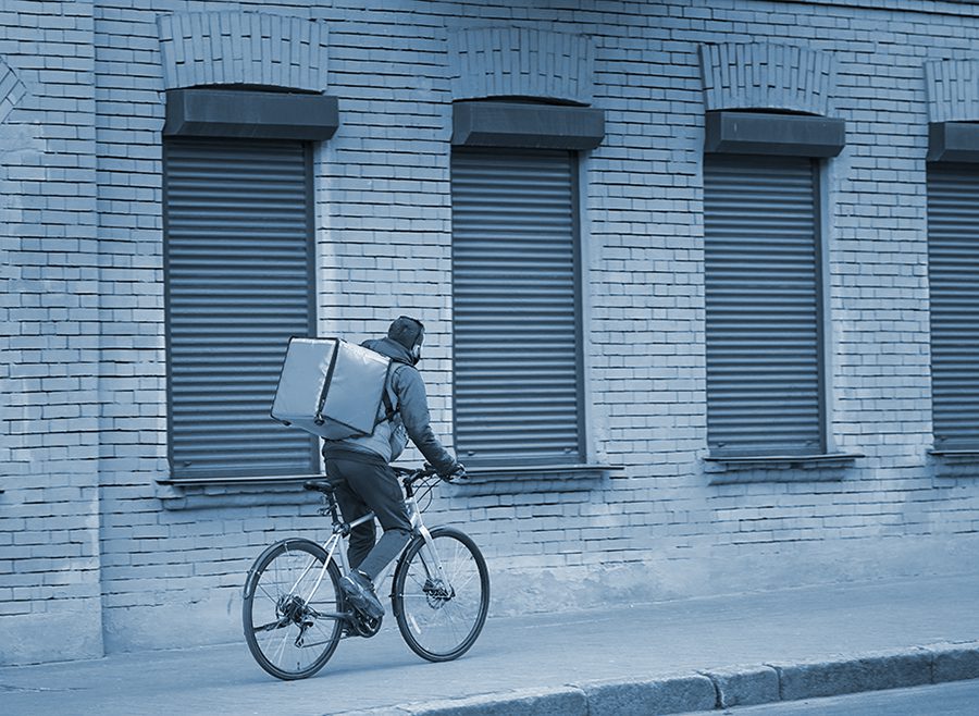 cyclist makes a delivery while riding on a city sidewalk