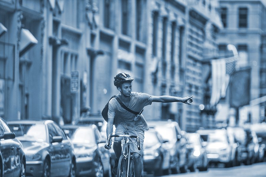 Cyclist makes a left hand turn signal on a busy city street.