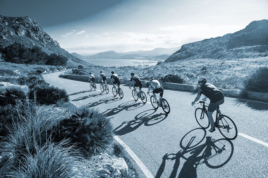 A group of bicyclist ride down a road in the desert.