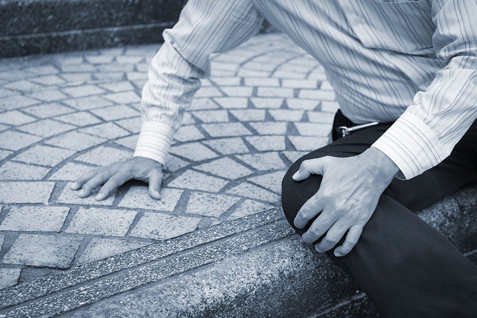 Man grabbing his knee after falling down on a sidewalk