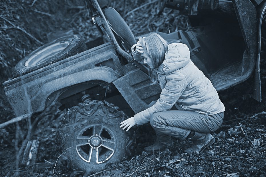 Shocked woman sits beside her ATV after a crash