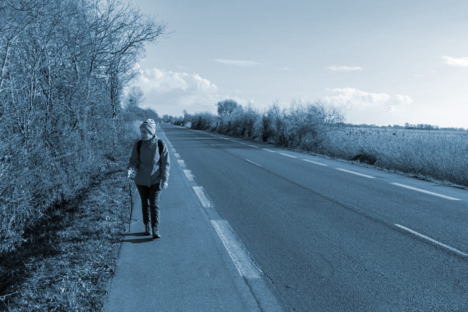 Girl walks on the shoulder of a country road.