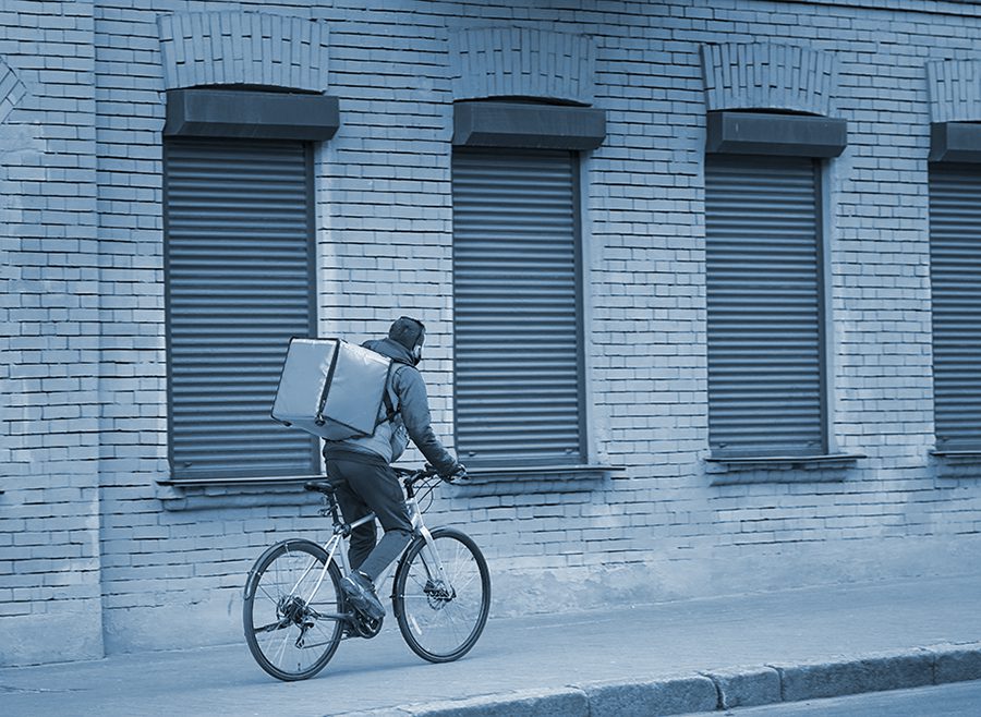Courier with red thermal backpack delivers pizza on bicycle