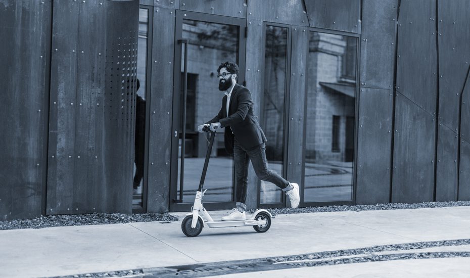 Hipster rides his e-scooter down a sidewalk