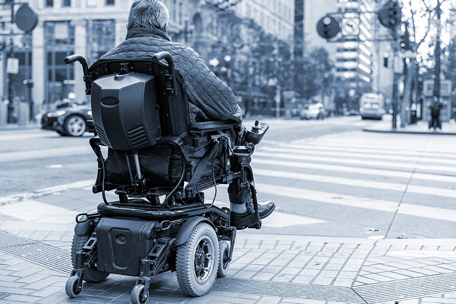 Man in a electric wheelchair crosses the street.