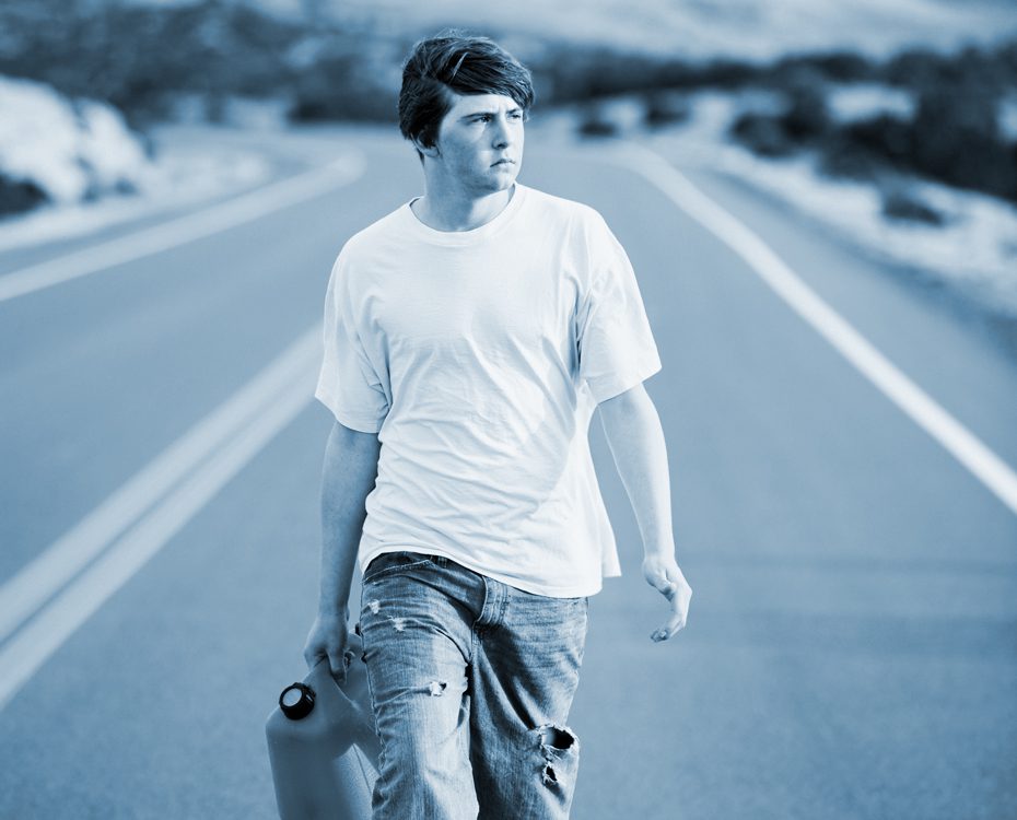 Man walks down a desert road with a gas can in hand