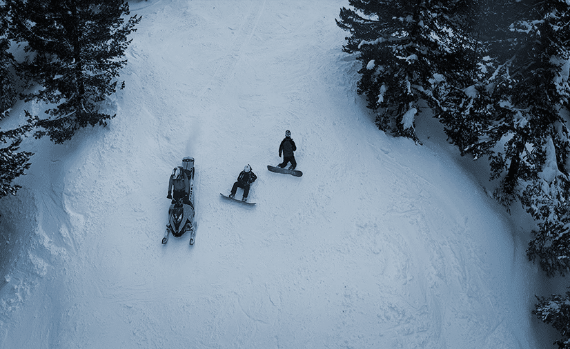 Two Snowboarders lay in the snow next to a snowmobile