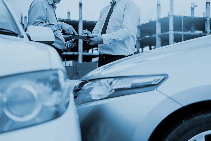 Insurance agent writing on clipboard while examining car after an accident