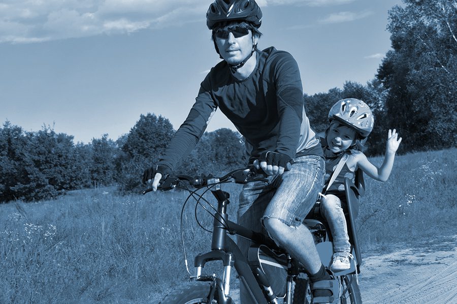 Dad and daughter ride bicycle by a field.