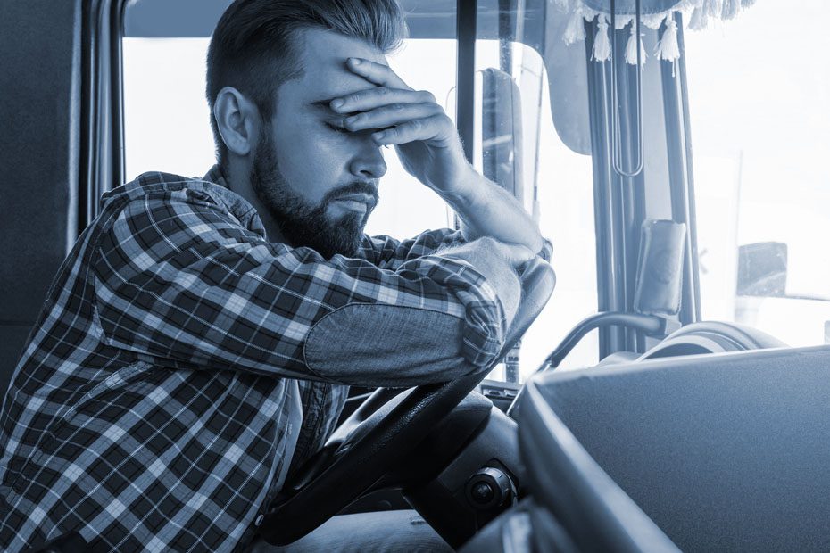 Exhausted trucker leans on steering wheel of the tuck while resting his face in is hand