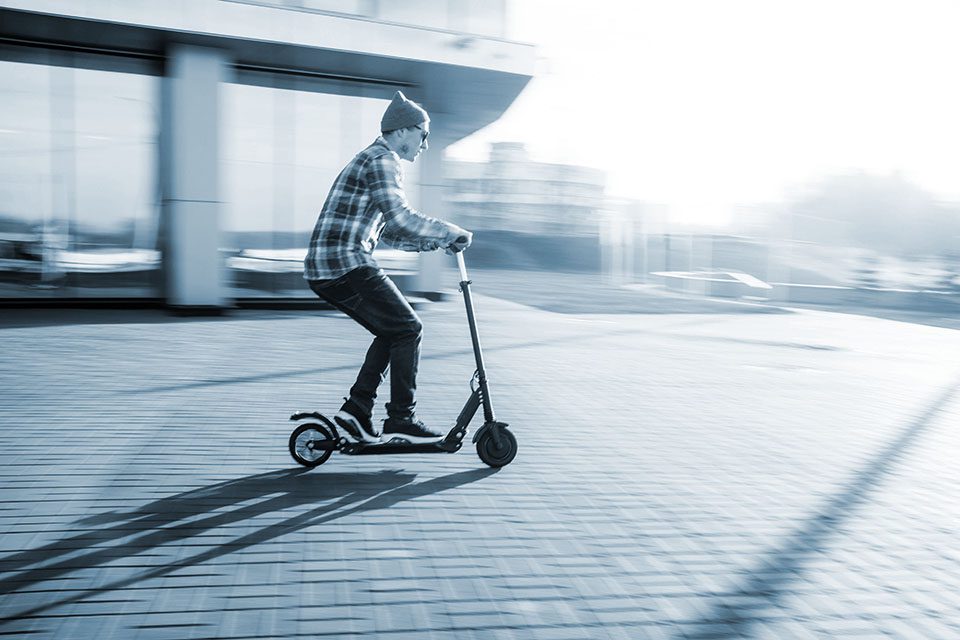 Man in flannel rides scooter across the courtyard area