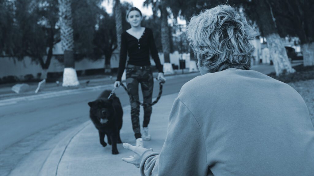 woman walks a black dog toward a trainer