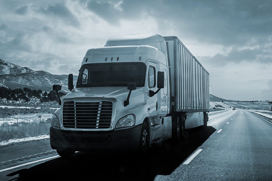 Semi-truck driving in the right lane on a desert highway.