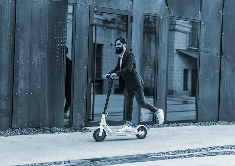 Hipster riding electric scooter on the sidewalk in front of run down buildings