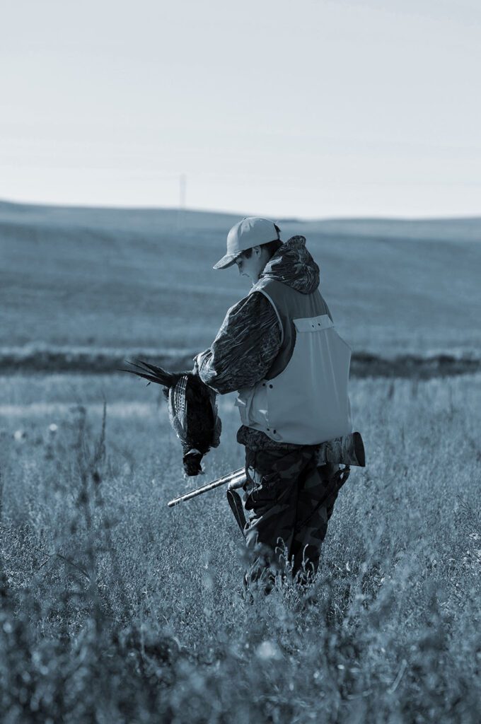 Hunter holds rifle and shot bird. 
