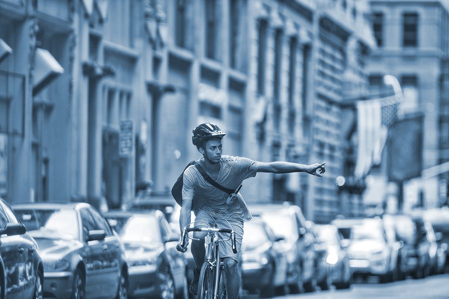 Man riding bicycle signals a left turn on a city street.