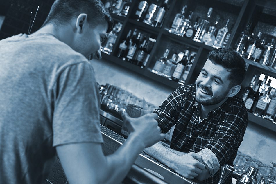 Bartender serves male customer at bar counter while smiling