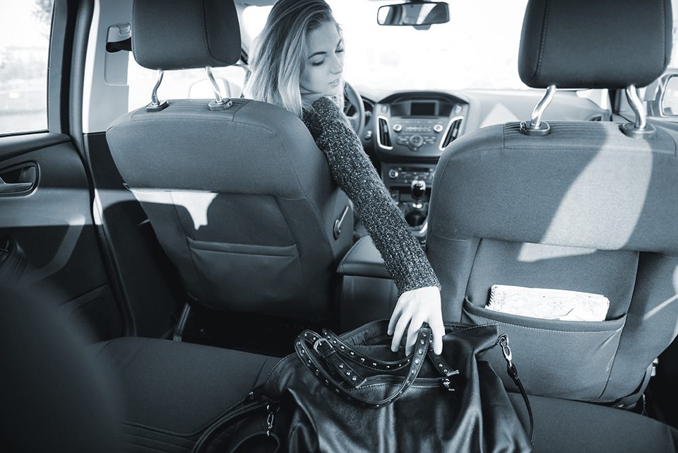 Young woman reaching purse from back seat - rear view