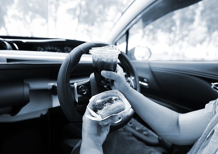 Driver hold and eat hamburger in car, dangerous and risk of accident.