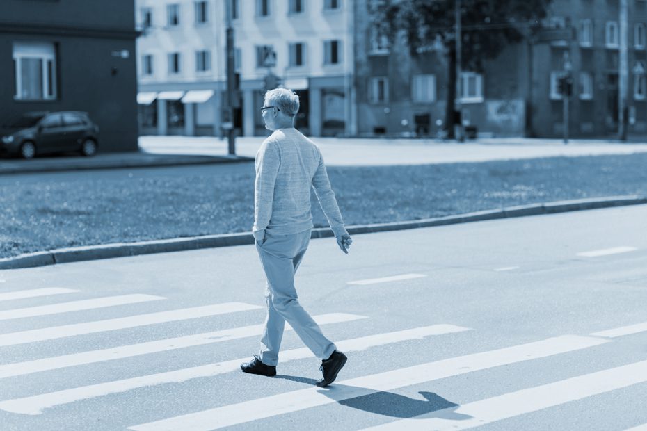 senior man walking along city crosswalk