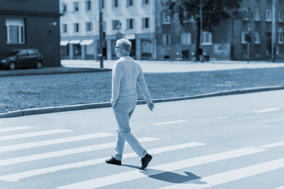 senior man walking along city crosswalk