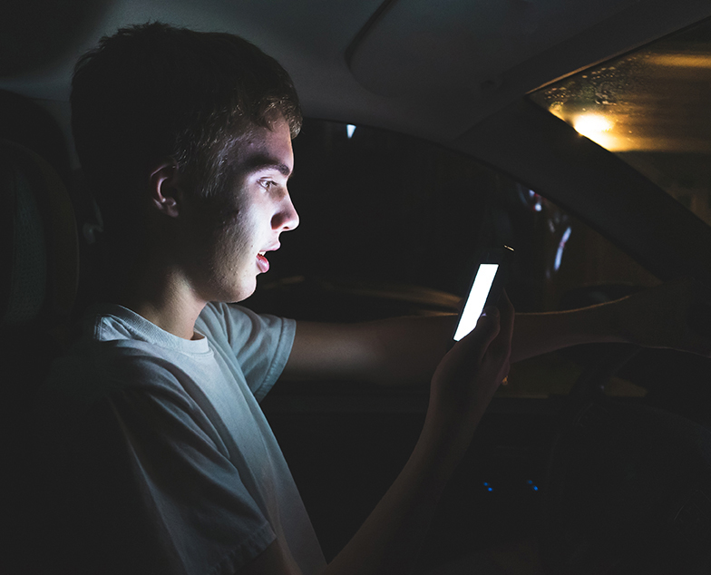 Teenager sitting in his parked car while using his smartphone