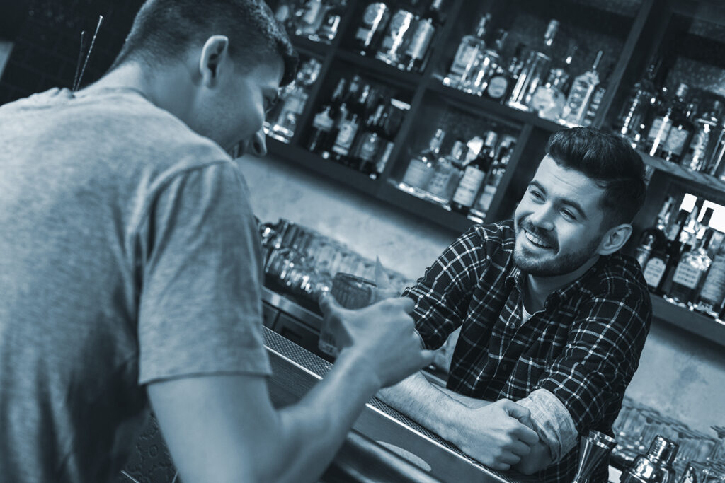 Young bartender standing at bar counter with customer laughing joyfully