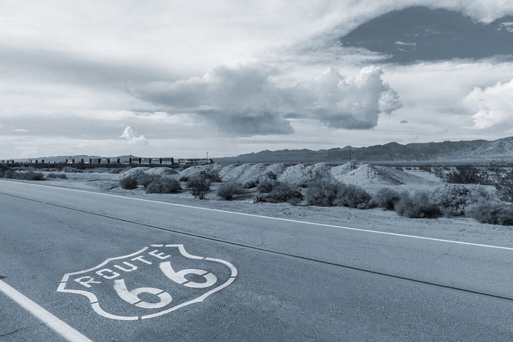 U.S. Route 66 highway, with sign on asphalt and a long train in background